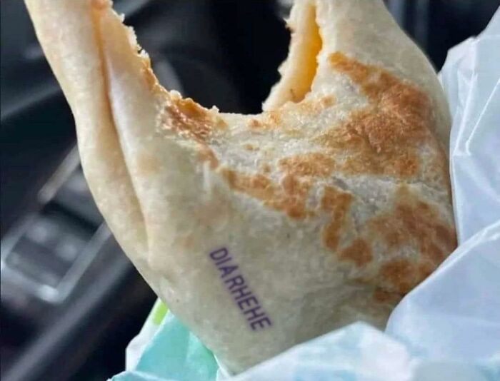 Cursed food burrito with humorous "DIARHEHE" label, partially eaten, wrapped in paper in a car setting.