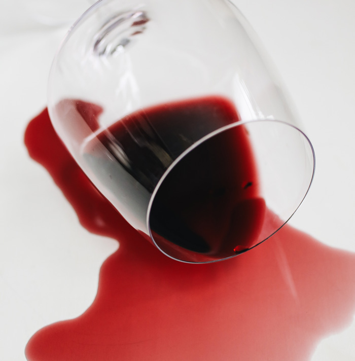 Spilled red wine from a tipped glass creating a dark stain on a white surface evoking scary facts and eerie vibes.