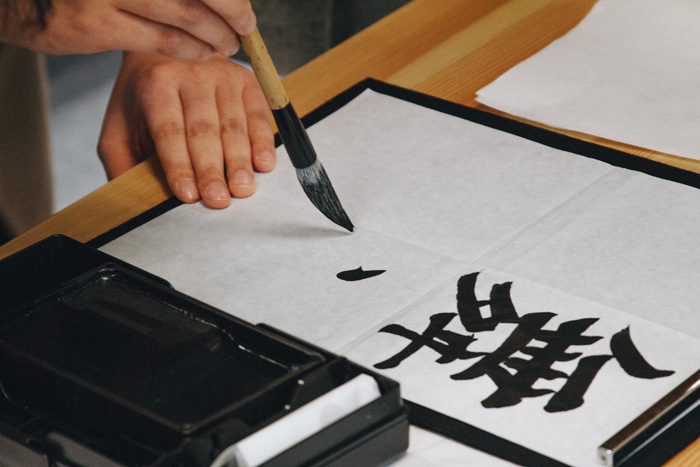 Person practicing Japanese calligraphy with brush on paper showcasing cultural diversity and beauty of the world.