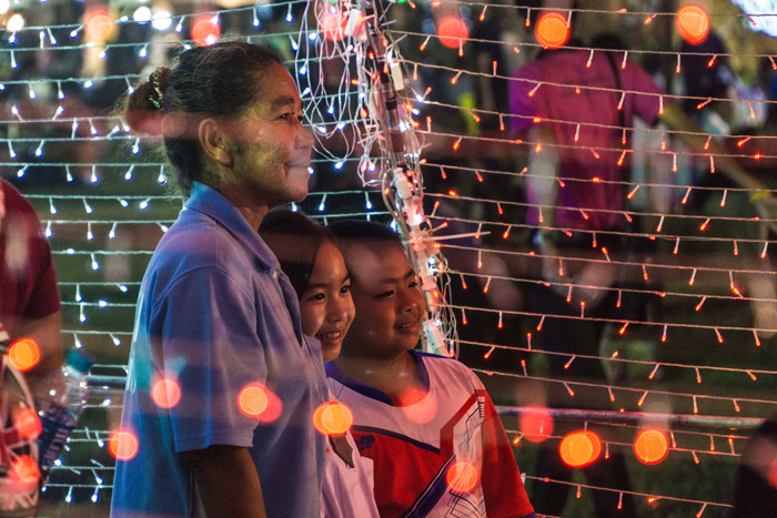 Woman with two children smiling under string lights in hra Nakhon Si Ayutthaya, Thailand, showcasing culture diversity and beauty.