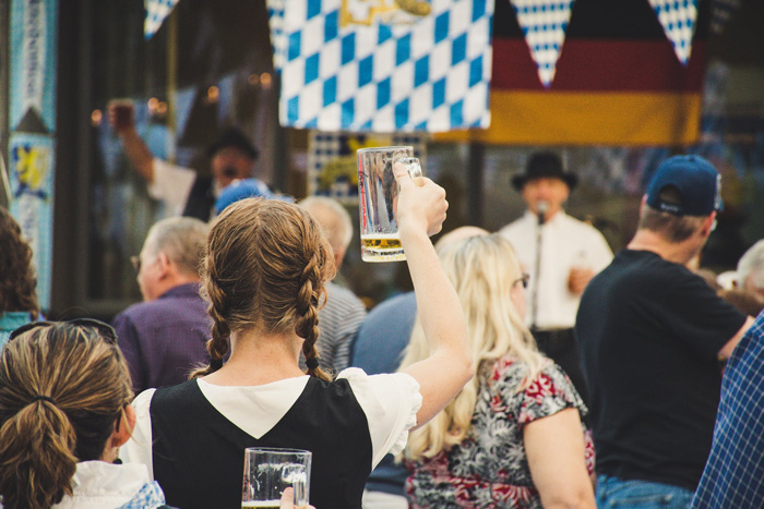 Woman in crowd raising beer glass celebrating culture diversity at a festive outdoor event with traditional decorations.