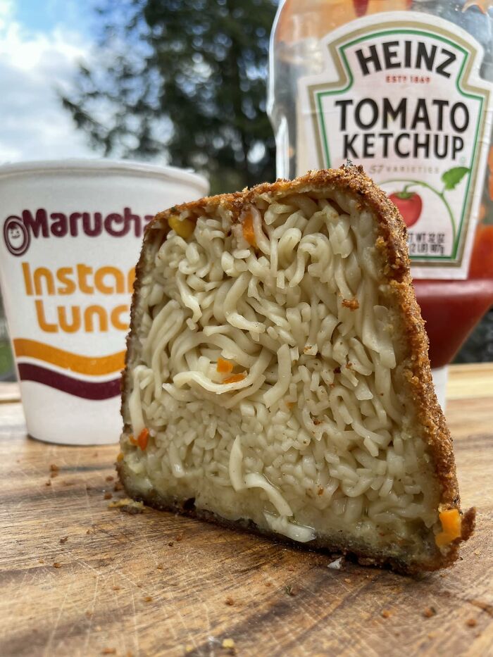 Cursed food: a deep-fried block of instant noodles with ketchup and instant lunch cup in the background.