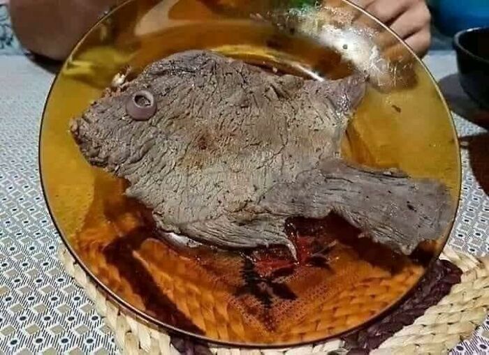 Cursed food resembling a steak shaped like a fish with an olive eye served on a plate.
