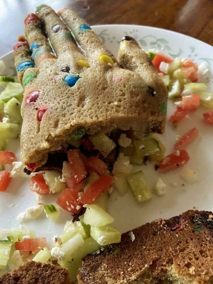 A bizarre, hand-shaped bread with candy pieces on a plate, resembling cursed foods that might turn your stomach.