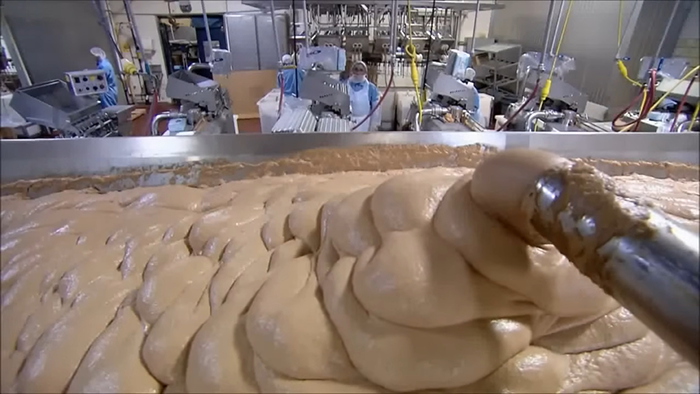 Large industrial food production line mixing dough with workers in protective clothing revealing behind-the-scenes food secrets.