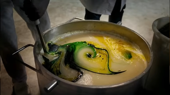 Large metal pot with a creamy yellow and green swirling mixture being stirred, showing disturbing behind-the-scenes secrets of popular meals.