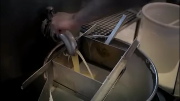 Hand pouring liquid ingredient into a metal machine, revealing disturbing behind-the-scenes secrets of popular meals.