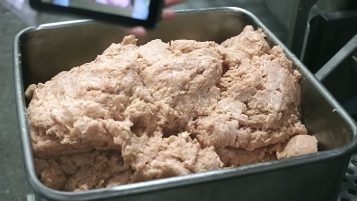 Raw processed meat mixture in a metal container revealing disturbing behind-the-scenes secrets of popular meals worldwide.
