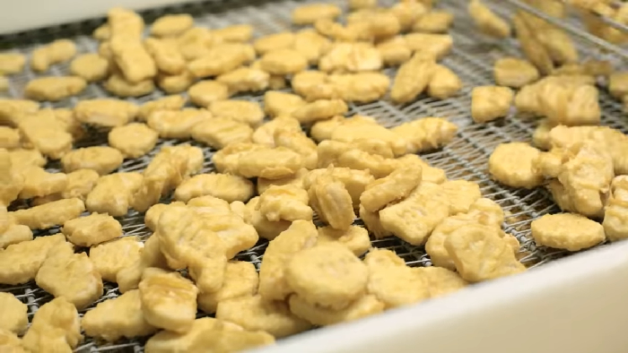 Frozen chicken nuggets on a conveyor belt during processing, revealing disturbing behind-the-scenes secrets of popular meals