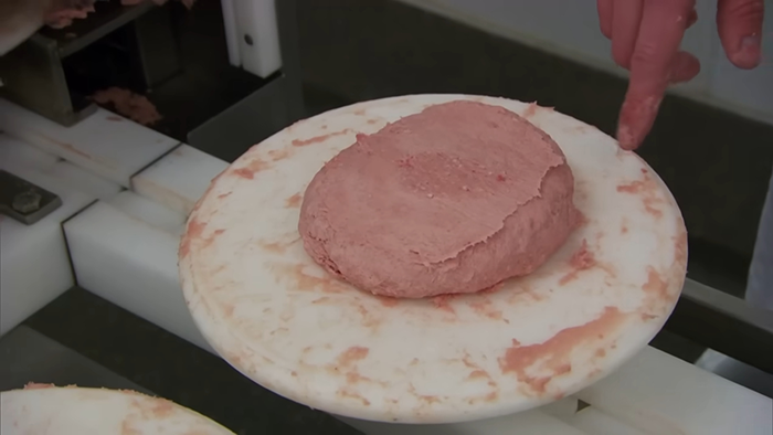 Processed meat being shaped by hand in a factory, revealing disturbing behind-the-scenes secrets of popular meals.