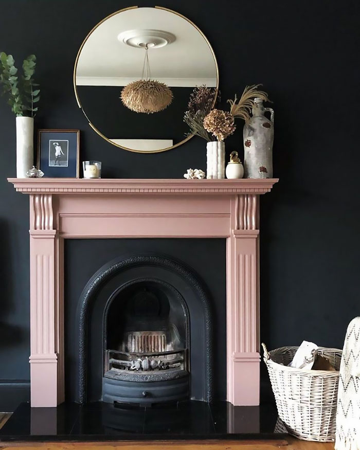 Dark living room featuring a pink fireplace mantel decorated with vases and a round mirror above it.