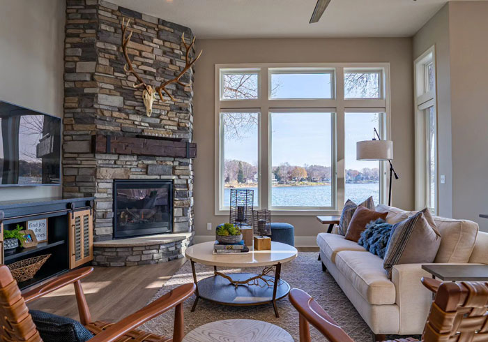Stone accent wall fireplace mantel with large moose antlers in a cozy living room overlooking a lake view.