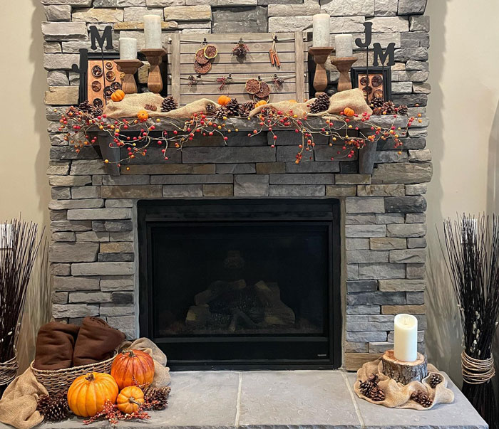 Stone fireplace mantel decorated with pumpkins, pinecones, candles, and autumn berries for a Halloween-themed hearth.