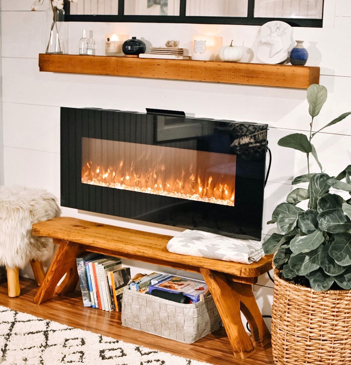 Black electric fireplace with wooden mantel in a light boho living room featuring cozy decor and greenery accents