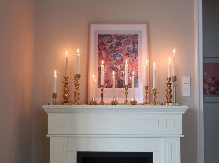 White wooden fireplace mantel decorated with multiple antique candle holders, creating a cozy hearth ambiance.