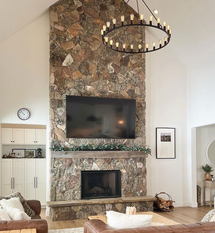 Stone backsplash fireplace mantel with mounted TV above, featuring rustic living room design and cozy hearth decor.