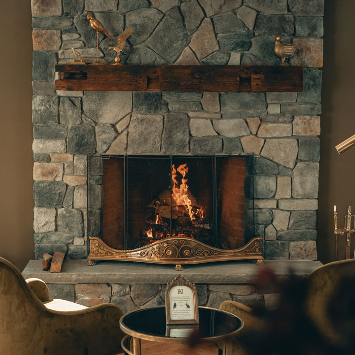Dark natural stone fireplace mantel with a burning wood fire, showcasing classic fireplace mantel ideas for a cozy hearth.