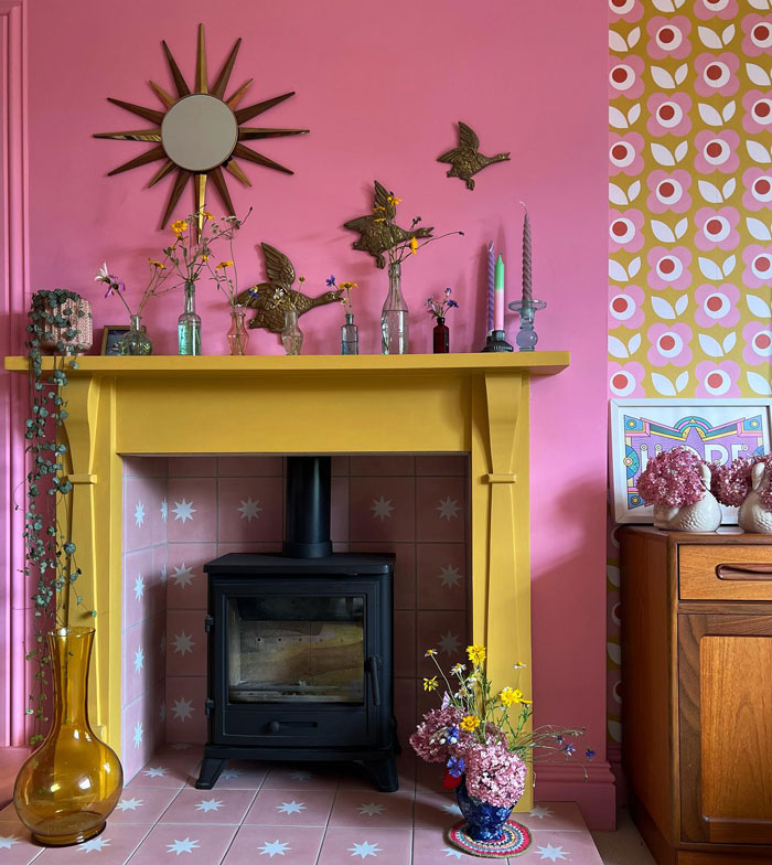 Colorful living room fireplace with a yellow painted mantel decorated with flowers and vintage accessories.