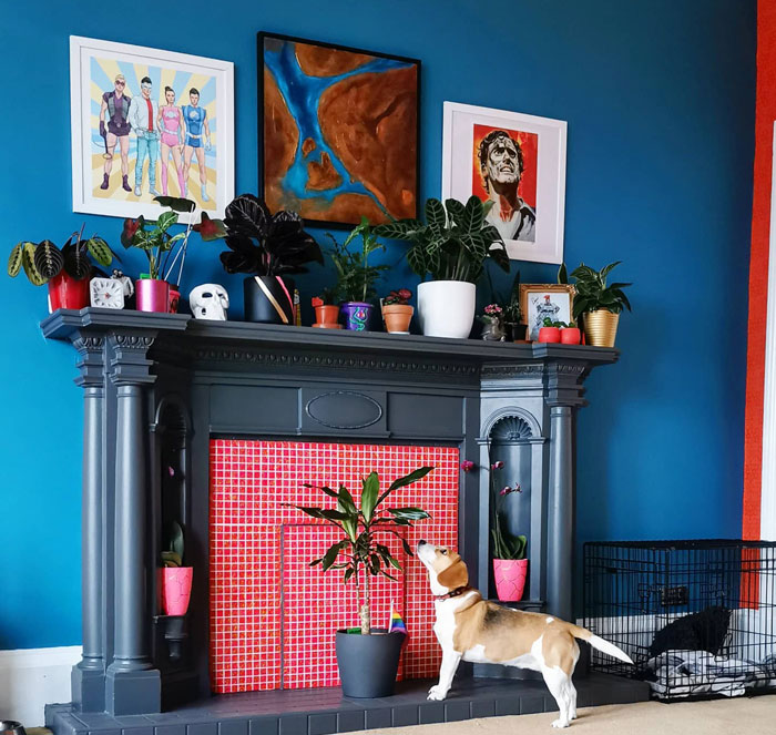 Blue living room with dark gray fireplace mantel, red tile hearth, various potted plants, and a dog exploring nearby.