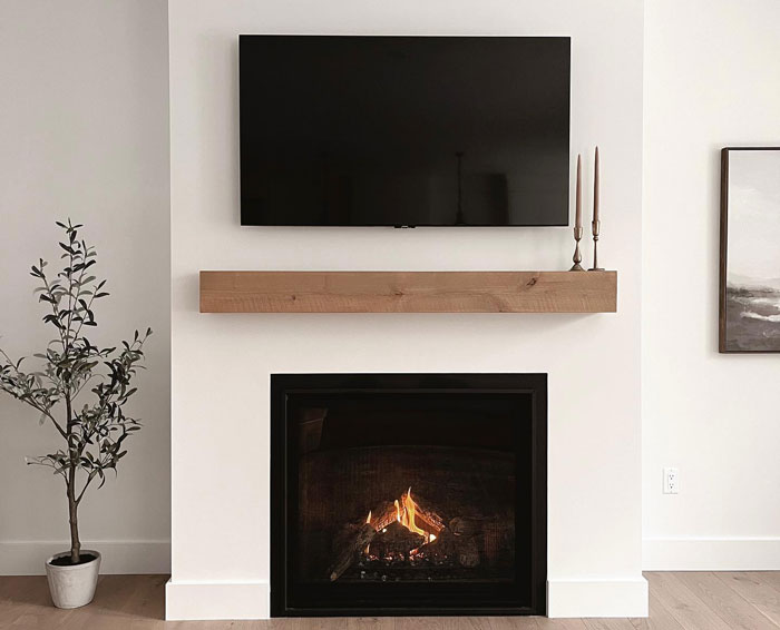 Minimalist white living room with a simple wooden fireplace mantel and a modern black TV above the hearth.