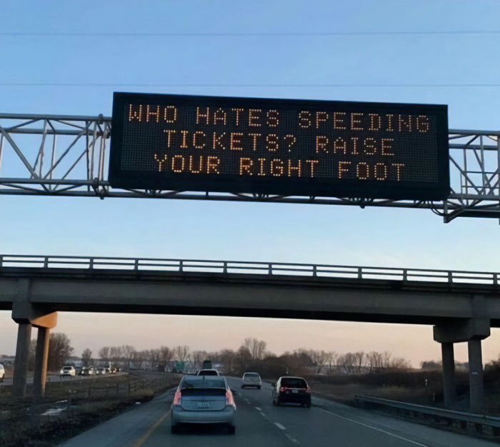 Highway sign with a humorous meme pun about speeding tickets, suggesting to "raise your right foot."