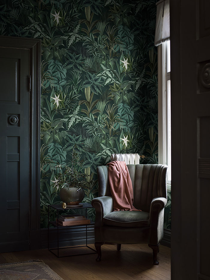 Dark room corner with biophilic accent wall, vintage armchair draped with a throw, showcasing elegant home decor ideas.