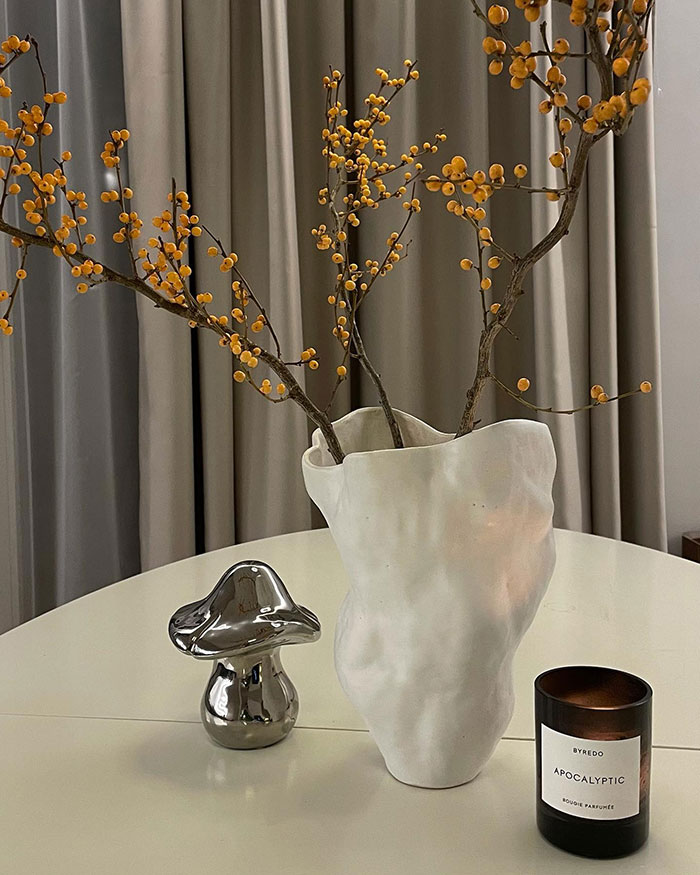 Handmade white vase with branches on table beside metallic mushroom and scented candle, showcasing home decor ideas and nowness.