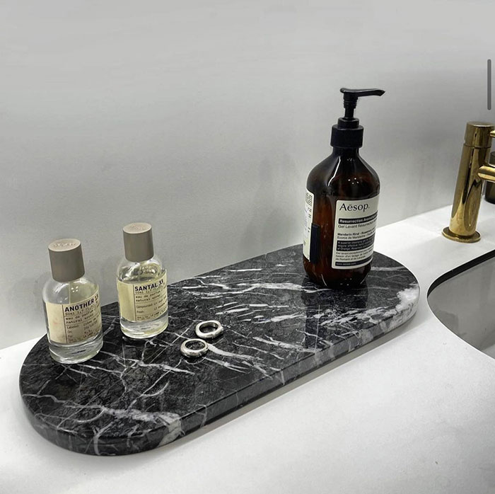 Cosmetics and jewellery arranged on a sleek black marble tray in a bathroom, showcasing modern home decor ideas.