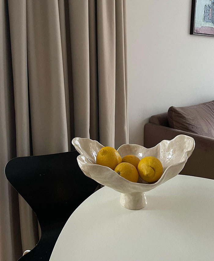 Four lemons arranged in a handmade ceramic bowl on a white table showcasing modern home decor ideas.