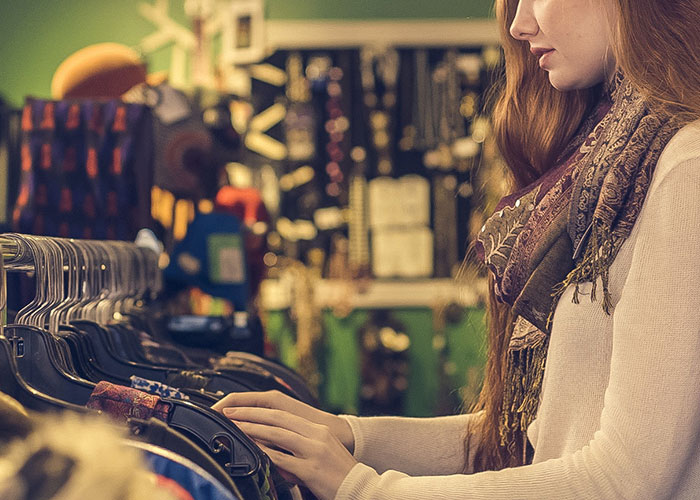 Young woman with red hair wearing a scarf, looking at clothes on hangers in a vintage shop, illustrating factors that make people look older.