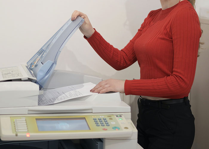 Person in a red sweater using a photocopier, illustrating habits that inevitably make people look older.