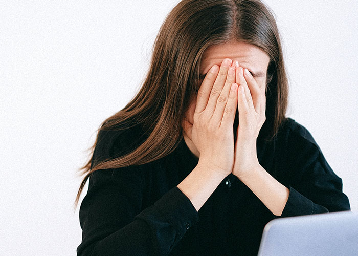 Young woman in black shirt covering face with hands, illustrating stress that can make people look older quickly.