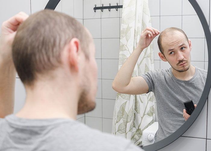 Man examining thinning hair in bathroom mirror, illustrating things that inevitably make people look older.