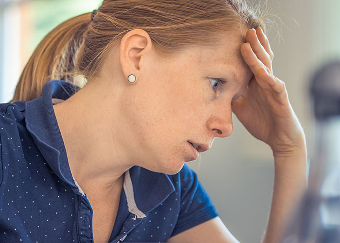 Young woman looking stressed with hand on forehead, illustrating things that inevitably make people look older.