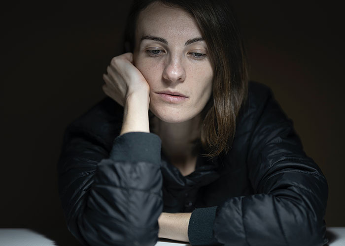 Young woman looking tired and pensive, showing signs that inevitably make people look older in dim lighting.