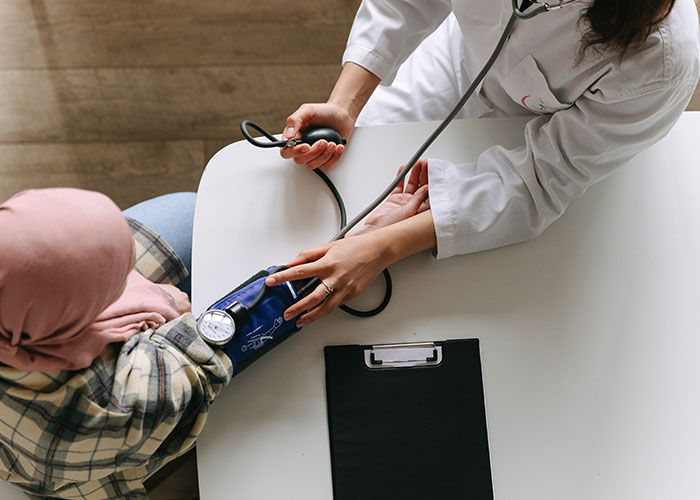 Doctor measuring blood pressure of patient wearing a headscarf in a clinical setting, illustrating factors that make people look older.