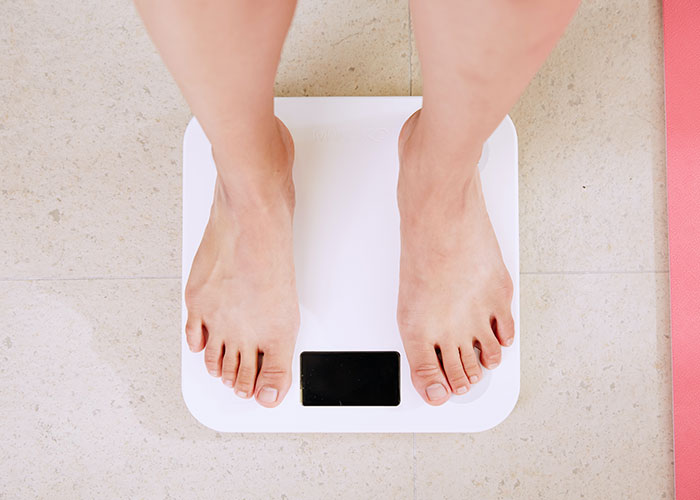 Bare feet standing on a digital scale on a tiled floor, illustrating factors that inevitably make people look older.
