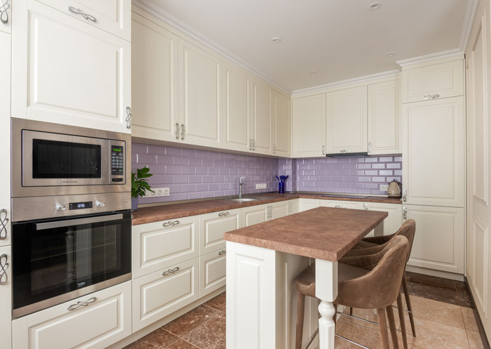 light kitchen with white cabinets, kitchen island with chairs and microwave with oven