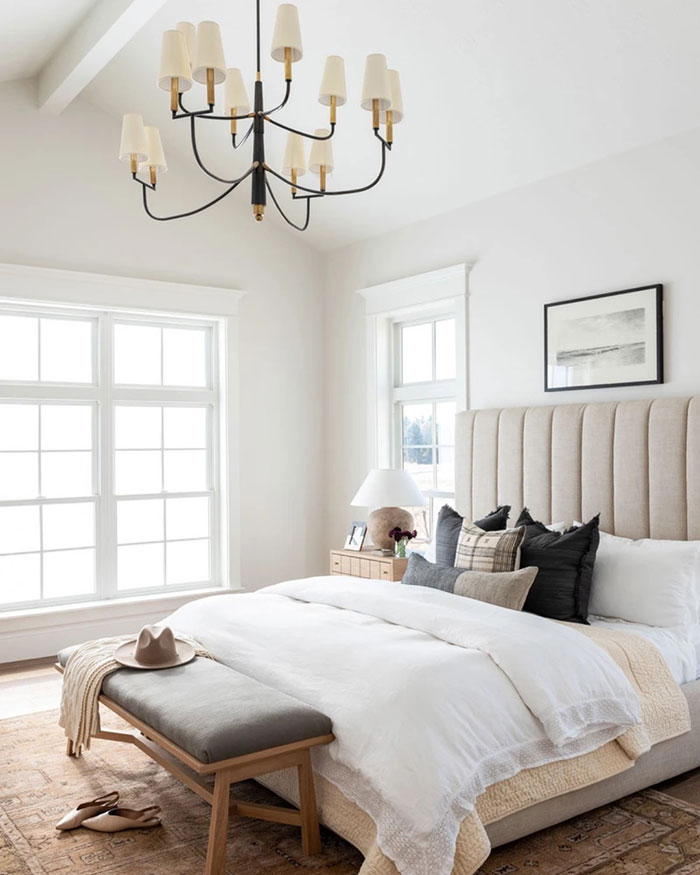 Soft palette master bedroom featuring a tufted headboard, layered bedding, modern chandelier, and cozy bench seating.