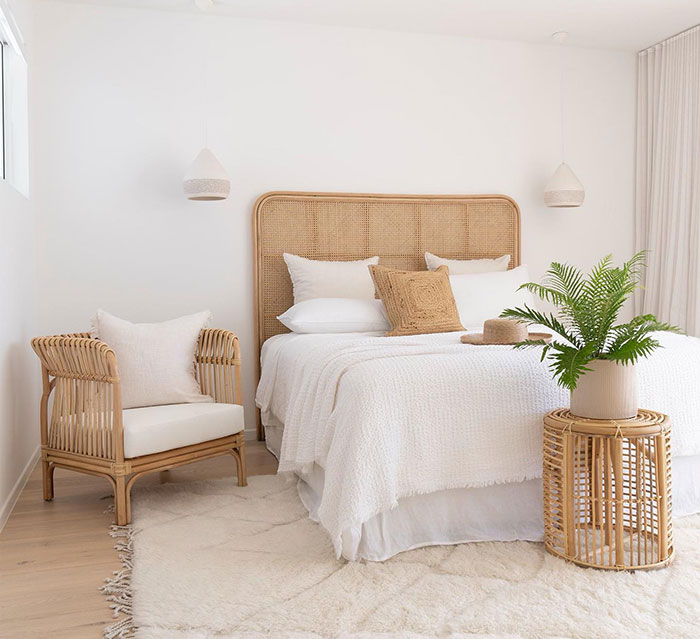 Bright master bedroom design with rattan furniture including headboard, chair, and side table in a cozy setting.