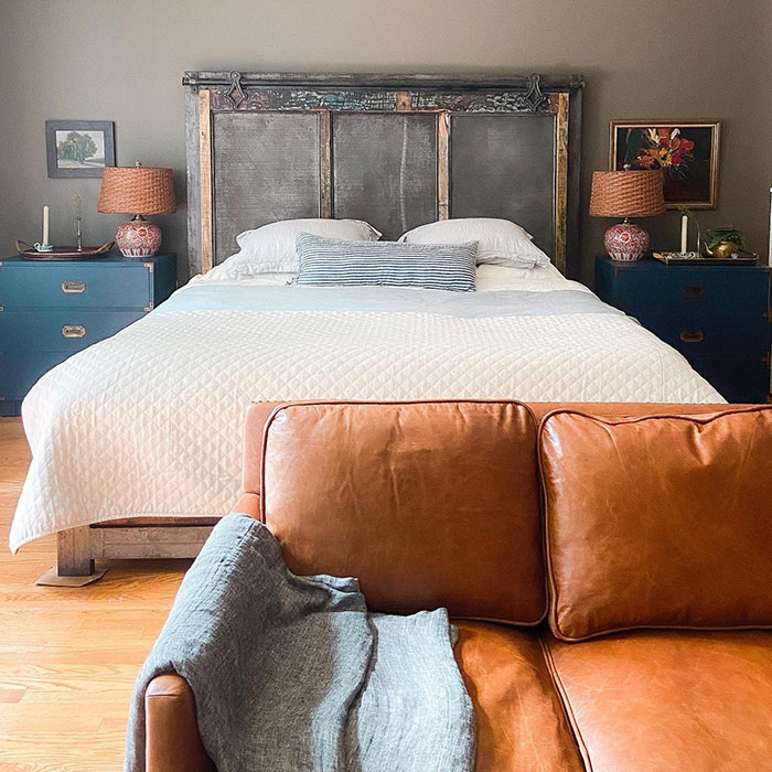 Cozy master bedroom design featuring vintage furniture with a leather sofa, quilted bedding, and blue nightstands.