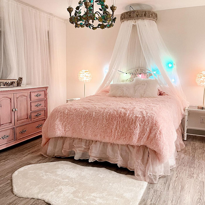 Pink princess master bedroom featuring a plush pink bedspread, sheer canopy, vintage dresser, and soft lighting for master bedroom ideas.