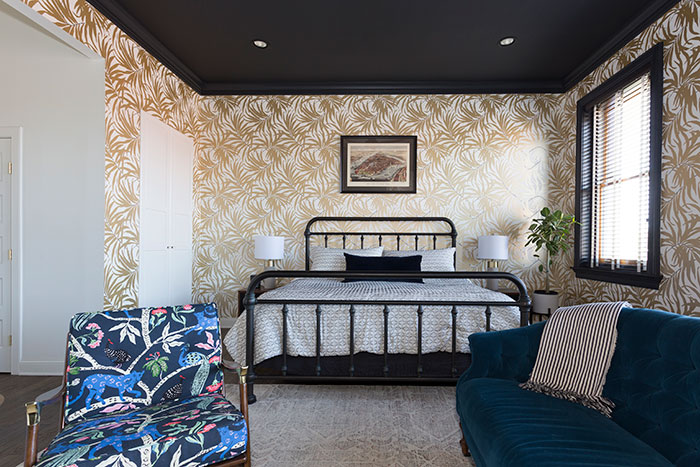 Colorful master bedroom with iron bed frame, patterned wallpaper, velvet sofa, and vibrant accent chair showcasing master bedroom ideas.