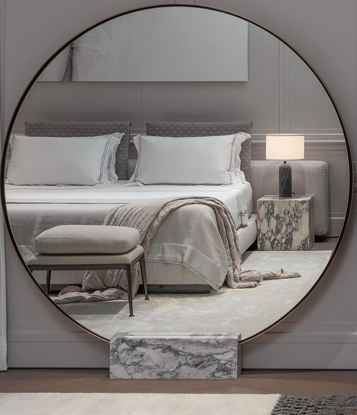 Cozy spacious master bedroom with a big round mirror, soft bedding, and elegant modern decor elements.
