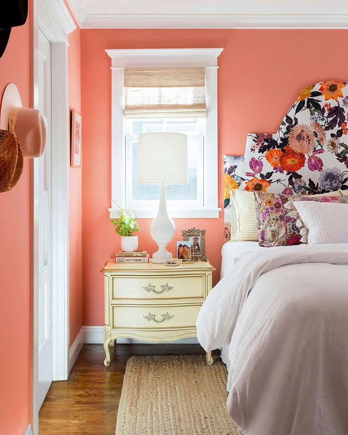 Colorful master bedroom ideas featuring a floral headboard, coral walls, vintage nightstand, and playful decor accents.