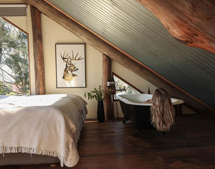 Clawfoot tub placed in a master bedroom with slanted ceiling and rustic wood beams, showcasing unique master bedroom ideas.