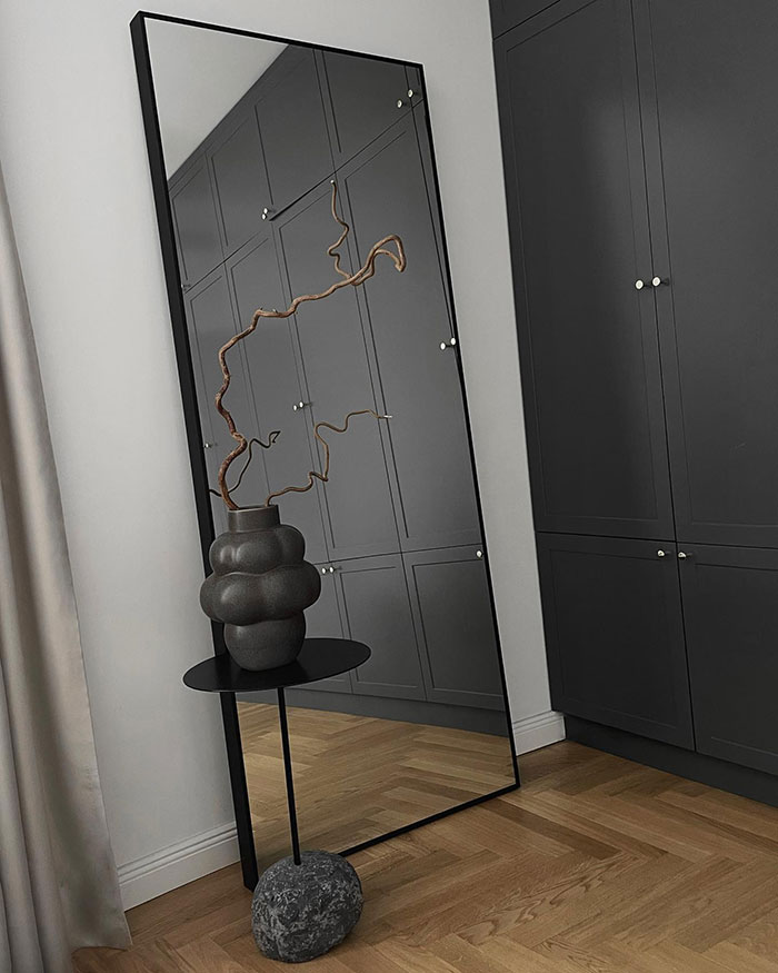 Corner mirror with modern black vase and minimalist bedroom design reflecting dark cabinets and wooden floor.