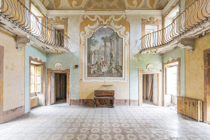 Abandoned ornate room with peeling paint, broken piano, and faded artwork in a post-apocalyptic world setting.
