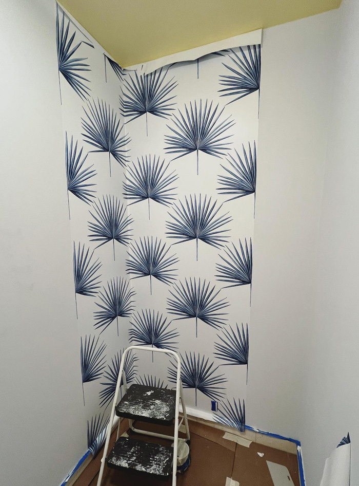 Partially applied removable wallpaper with blue palm leaf pattern on a white wall, showcasing stylish decor ideas.