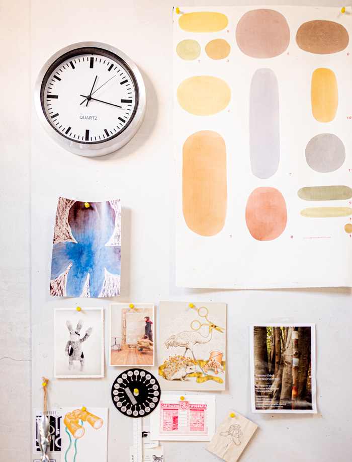 Wall with various wallpaper samples and decor ideas pinned under a round wall clock for removable wallpaper decor.
